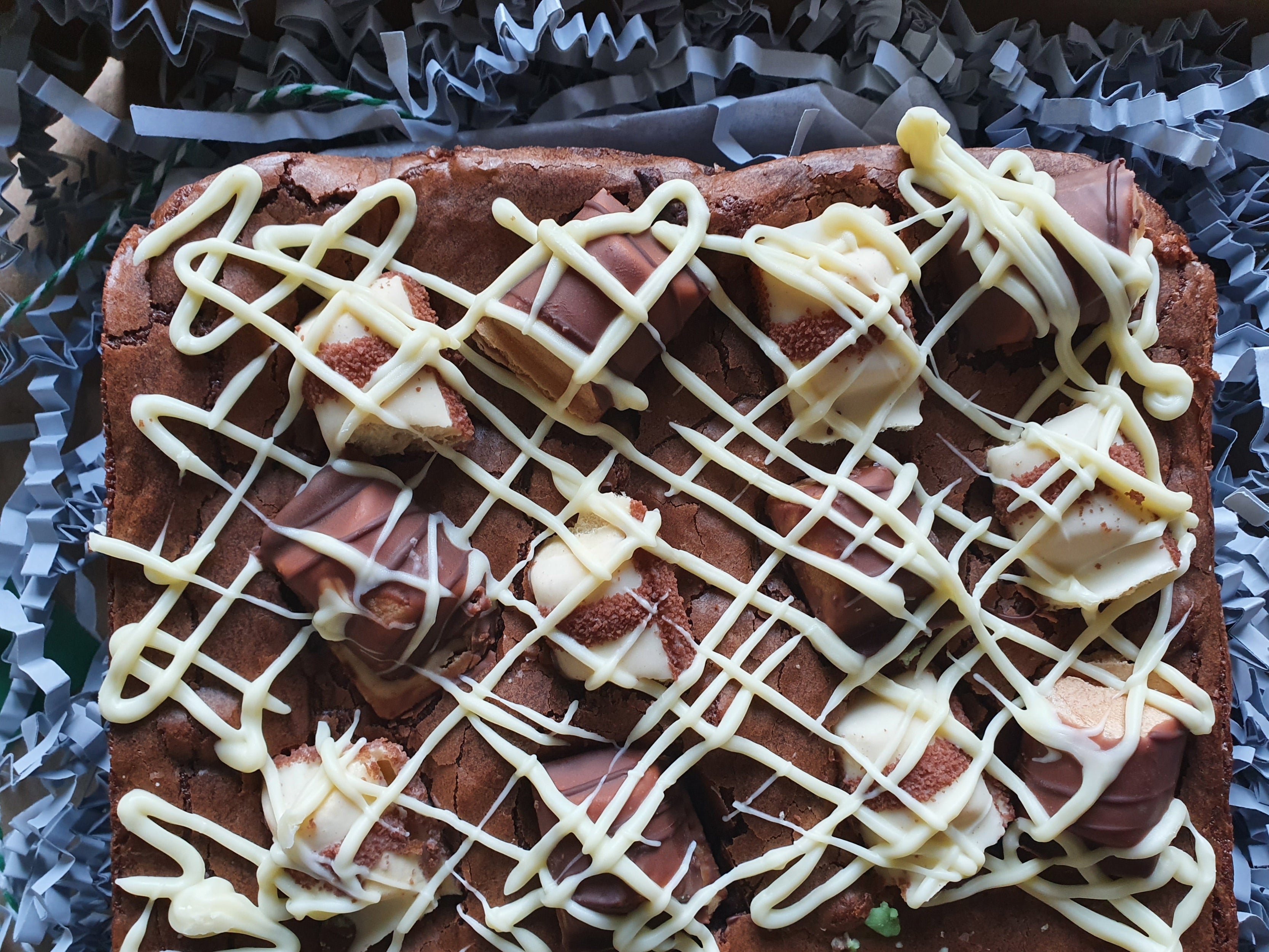 Brownie with white chocolate drizzle on a silver foil background